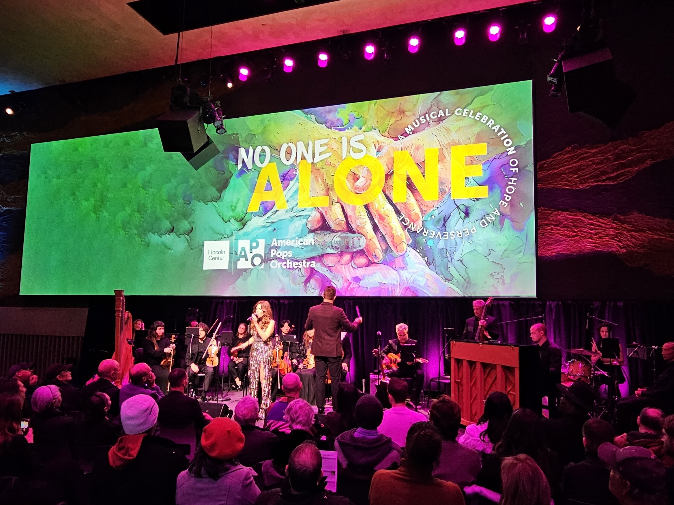 No One Is Alone banner with Maestro Luke Frazier conducting Joely Fischer